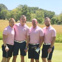 4 team members pose for a picture on the green in pink shirts